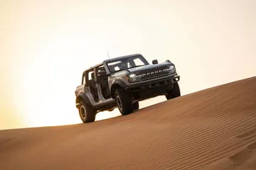 Vista lateral de un Ford Bronco superando duna en un ambiente desértico.