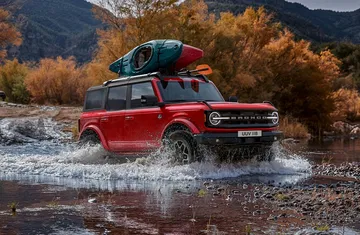 Ford Bronco rojo cruzando un río con equipaje en el techo.