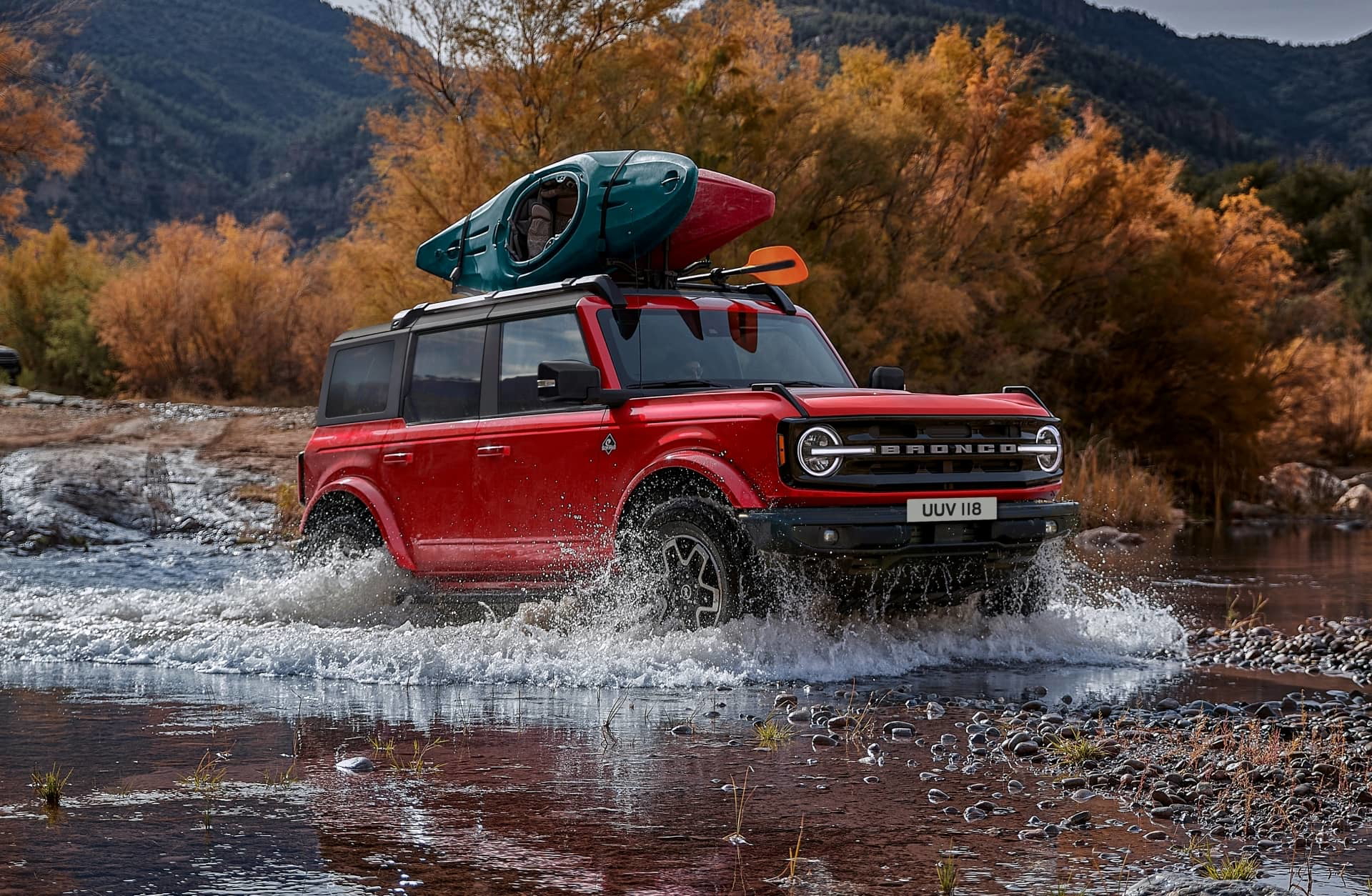 Ford Bronco rojo cruzando un río con equipaje en el techo.