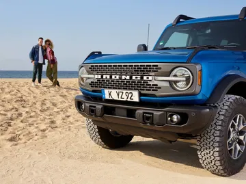 Vista lateral y delantera del Ford Bronco en color azul frente a la playa.