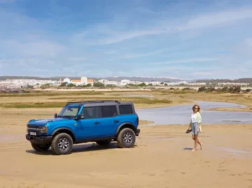 Vista lateral de un Ford Bronco azul circulando por la playa