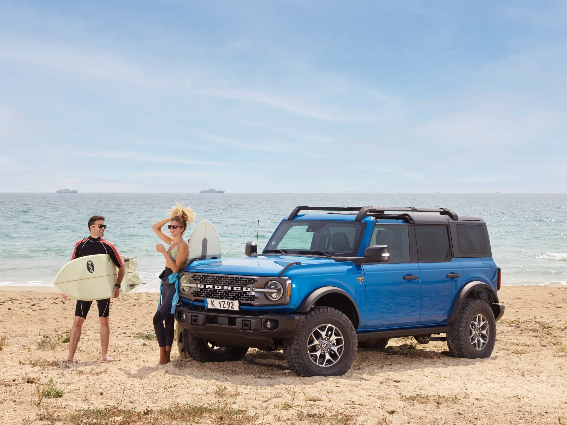 Vista lateral de un Ford Bronco azul con techo de lona junto a la playa.