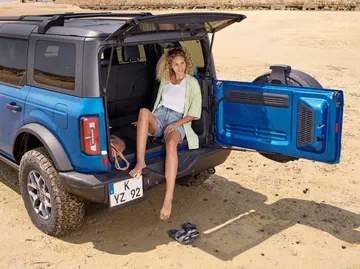 Imagen de Ford Bronco con puerta trasera abierta y una mujer sentada en el borde.