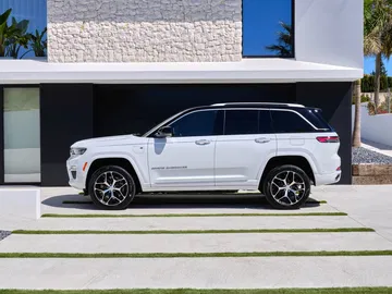 Vista lateral del Jeep Grand Cherokee estacionado frente a una residencia moderna.