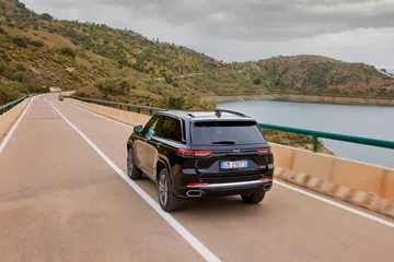 Vista lateral del Jeep Grand Cherokee rodando en carretera próxima a un lago.