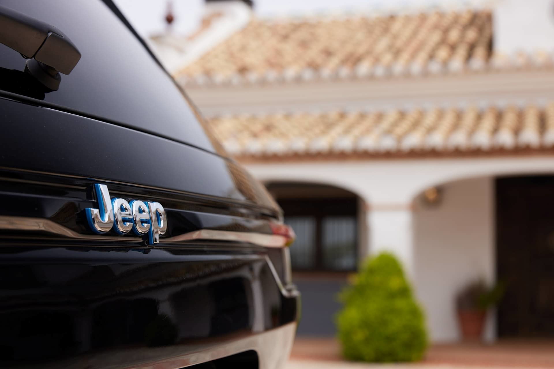 Enfoque en el emblema frontal del Jeep Grand Cherokee, con un borroso fondo residencial.
