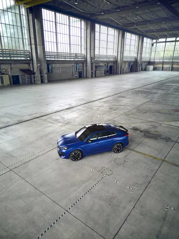 BMW X2 mostrado en perfil lateral en una nave industrial, destacando su diseño dinámico.
