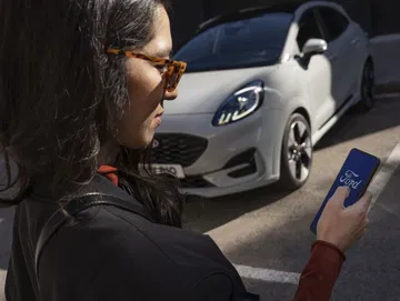 Una mujer opera su smartphone delante de un Ford Puma estacionado.