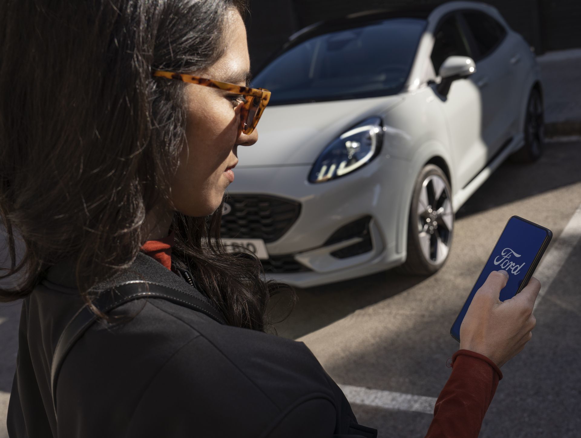 Una mujer opera su smartphone delante de un Ford Puma estacionado.