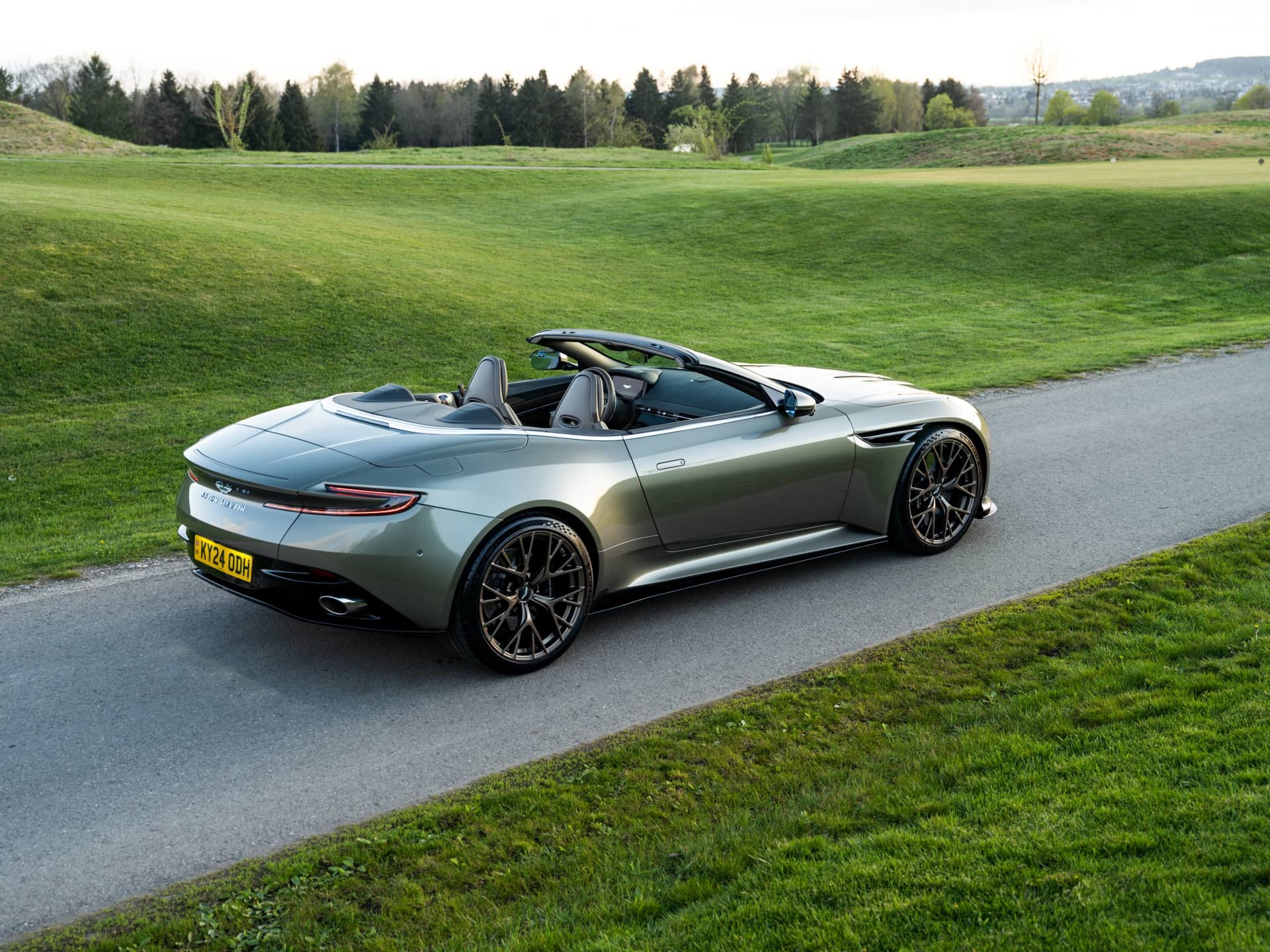 Aston Martin DB12 Volante en vista lateral y trasera, mostrando su elegante diseño y capota abierta.