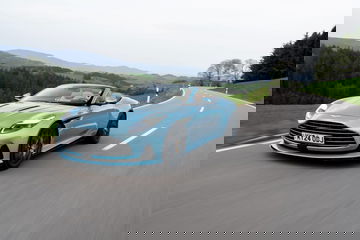 Vista dinámica del Aston Martin DB12 Volante en carretera, destacando su diseño y aerodinámica.