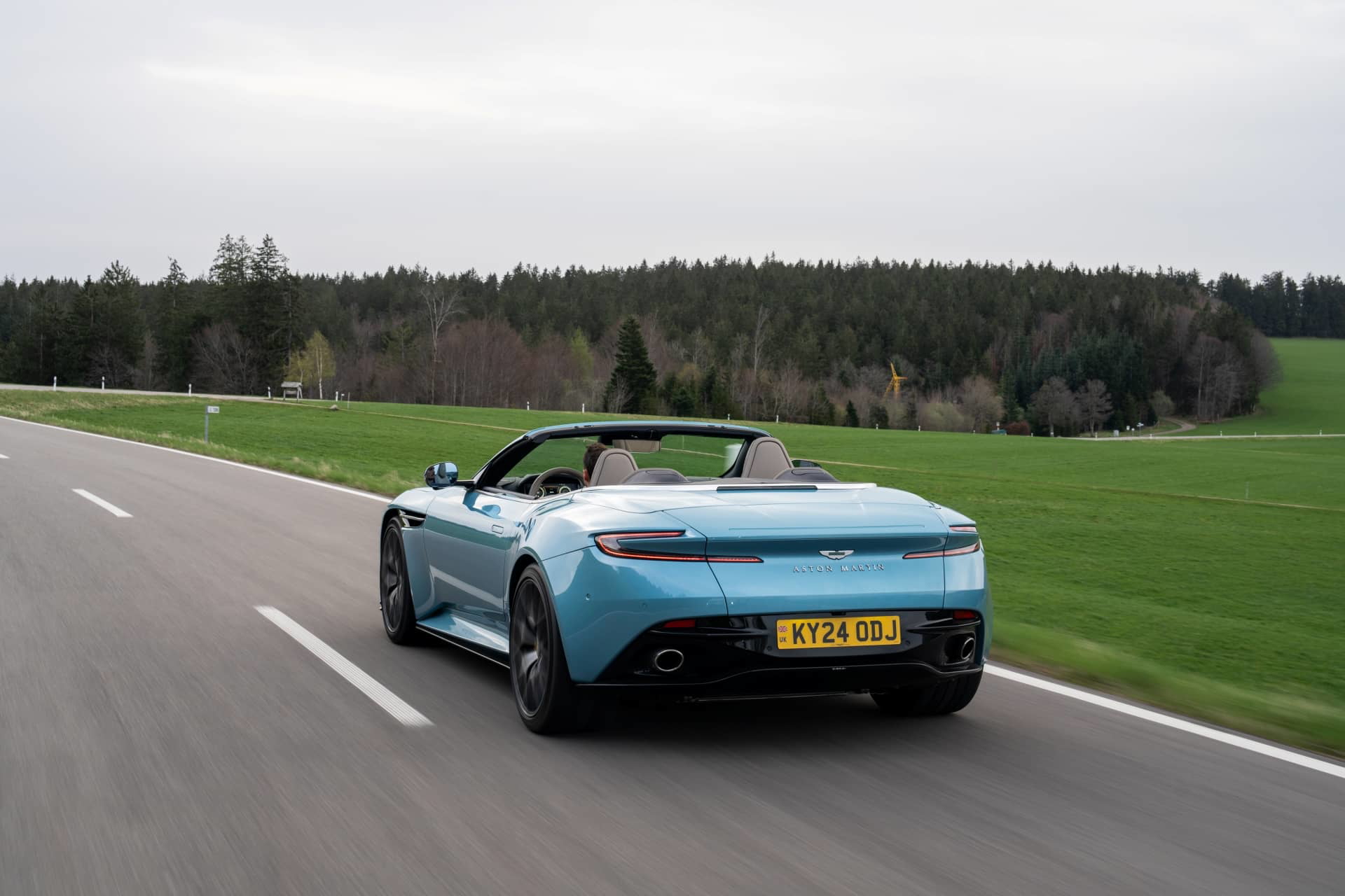 Vista dinámica del Aston Martin DB12 Volante en carretera, énfasis en diseño trasero