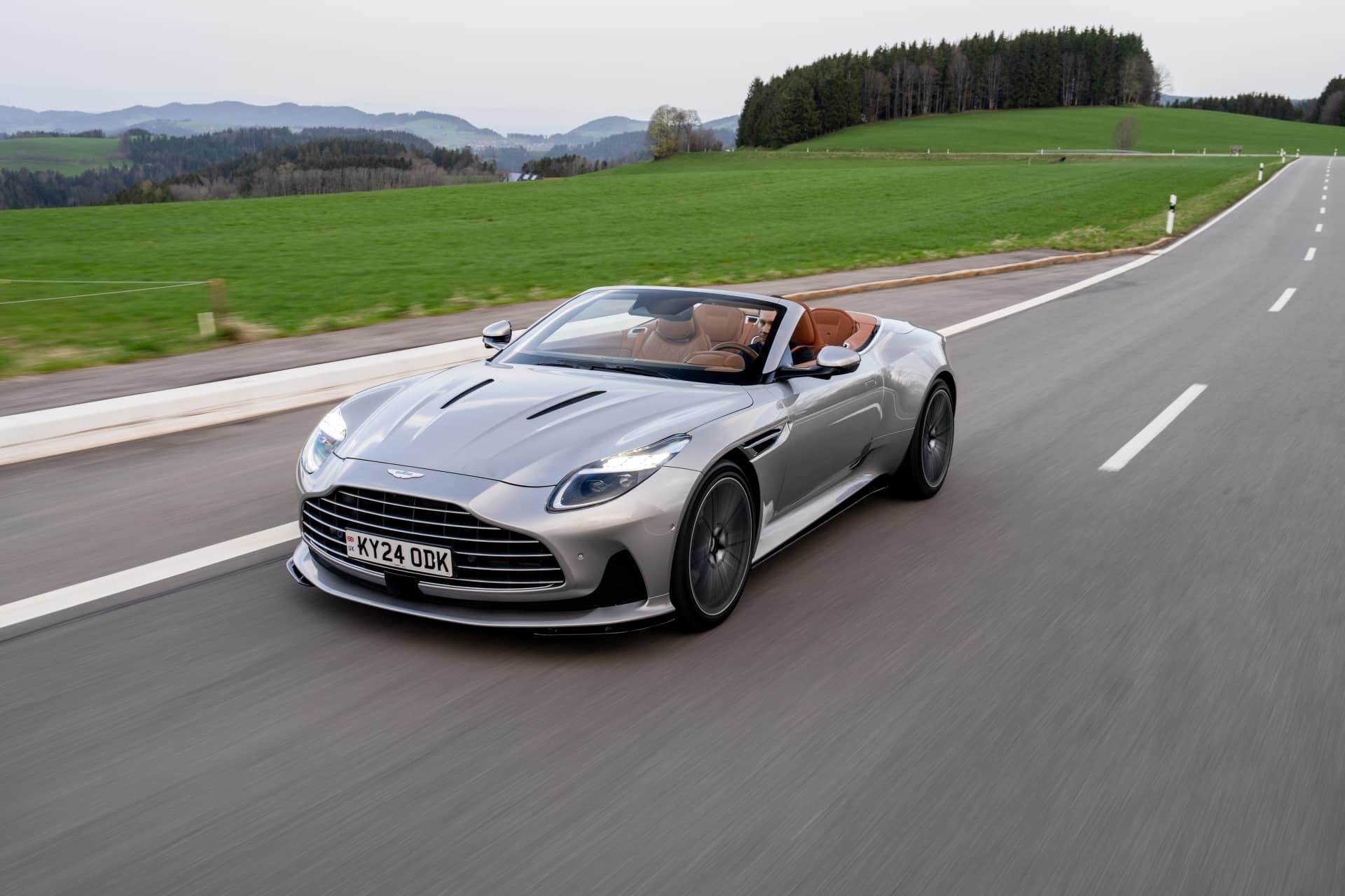 Aston Martin DB12 Volante en movimiento, capturado desde el frente y lado, diseño elegante.
