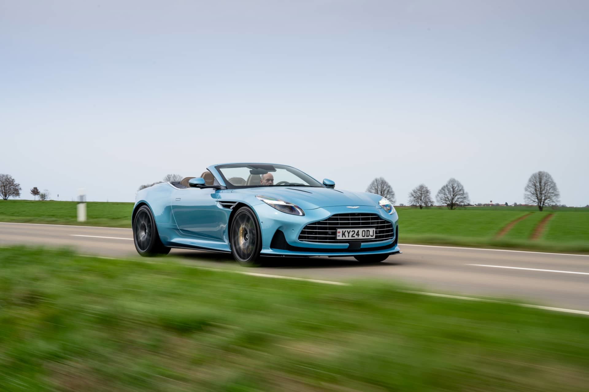 Vista dinámica del Aston Martin DB12 Volante en carretera, destacando su diseño y aerodinámica.
