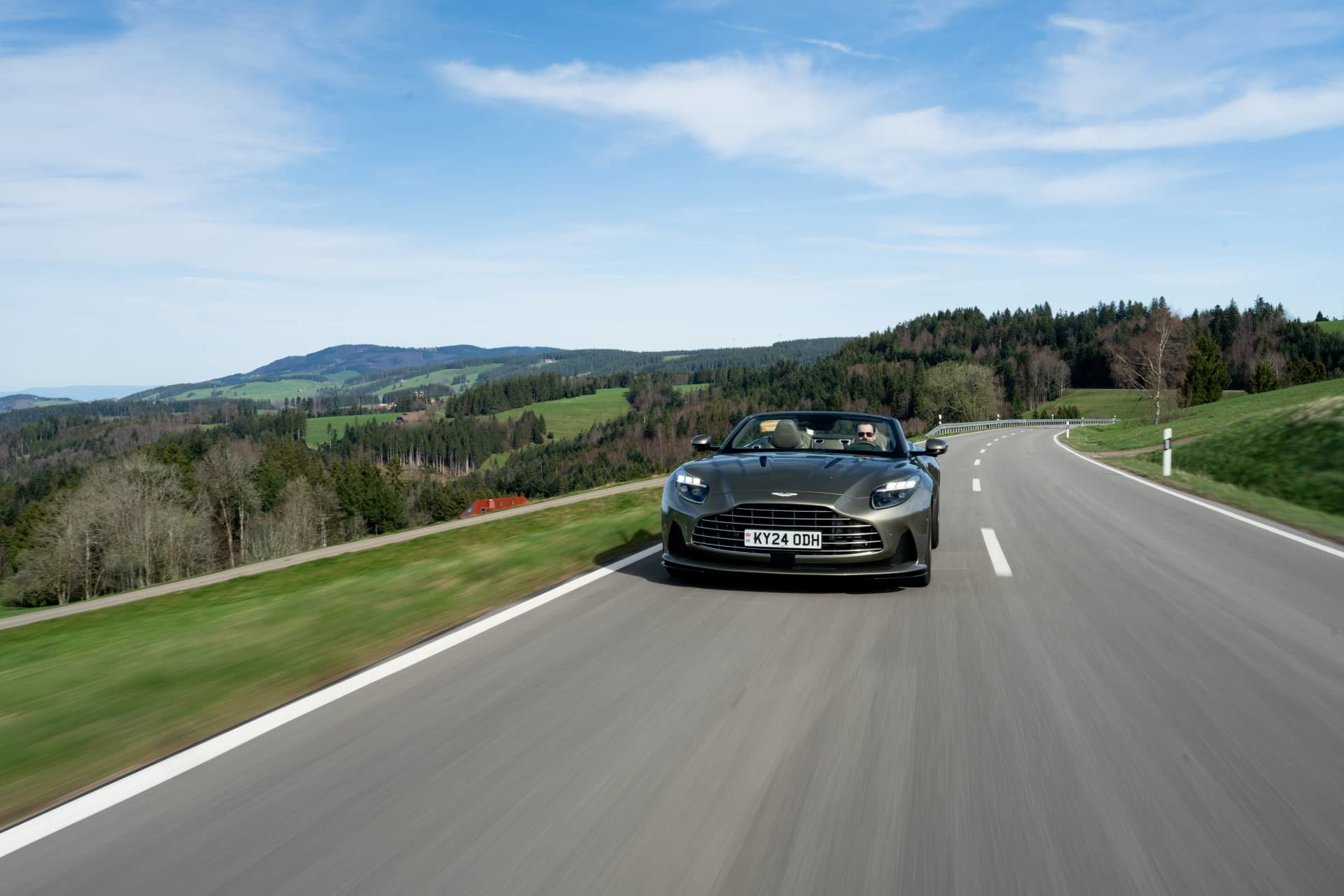 Vista dinámica del Aston Martin DB12 Volante en carretera, mostrando su diseño frontal y líneas laterales.