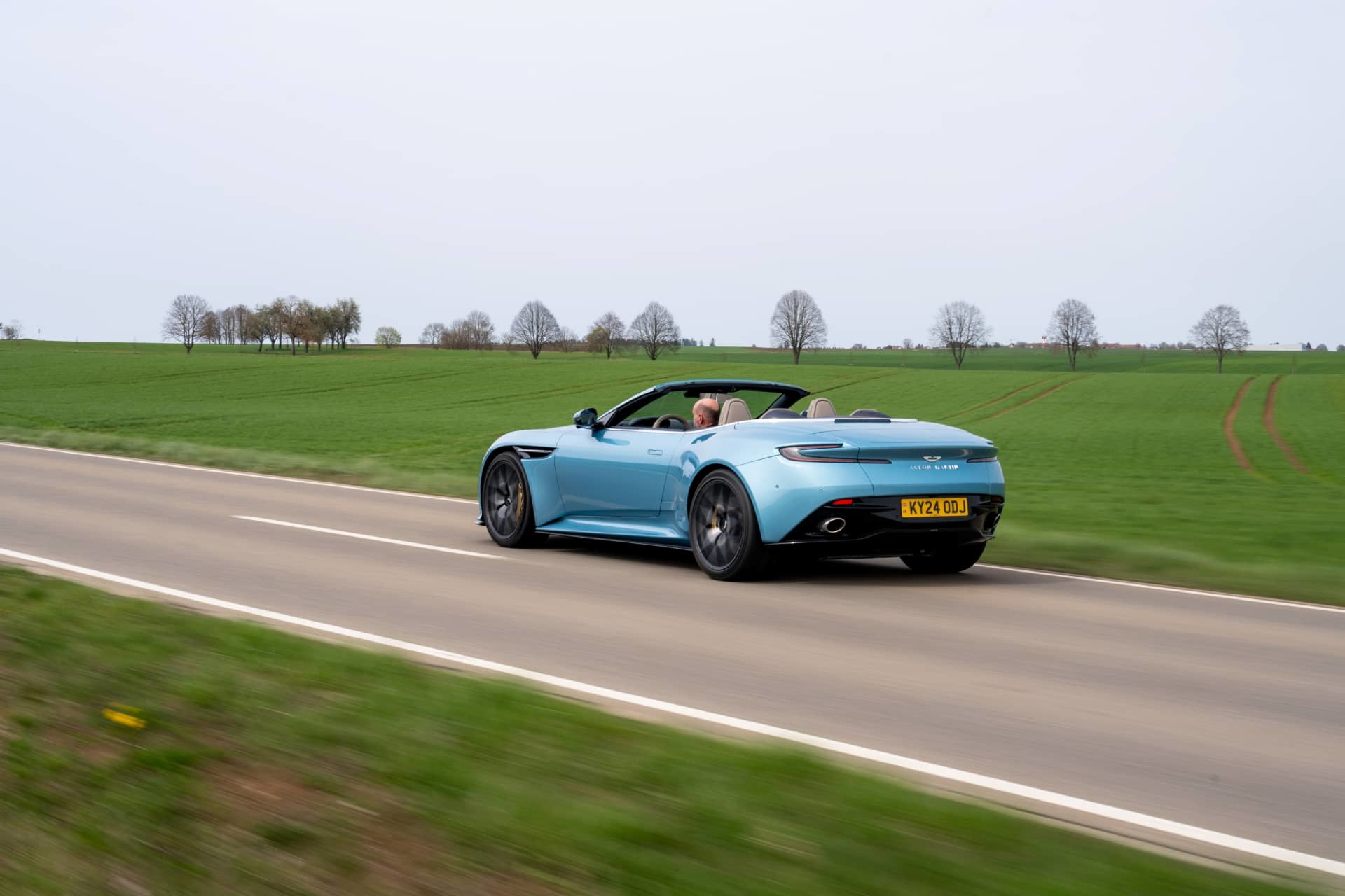 Vista lateral del Aston Martin DB12 Volante en movimiento, mostrando su elegante silueta.