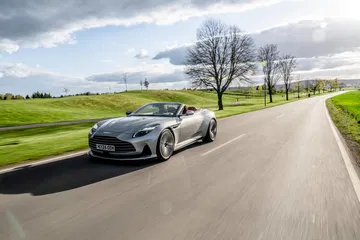 Vista dinámica del Aston Martin DB12 Volante en carretera, destacando su diseño y fluidez.