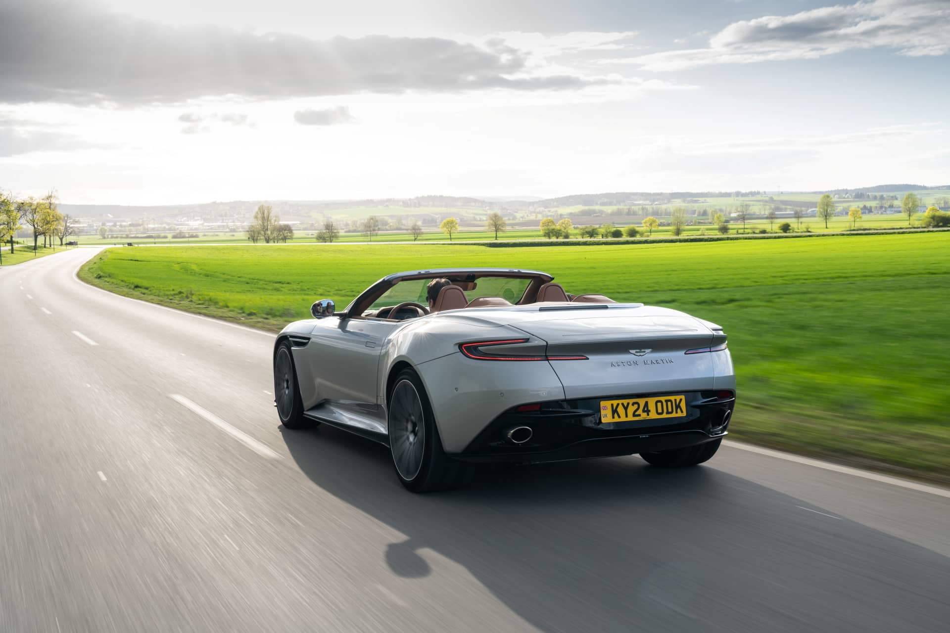 Vista dinámica del Aston Martin DB12 Volante en carretera, mostrando su elegante silueta.