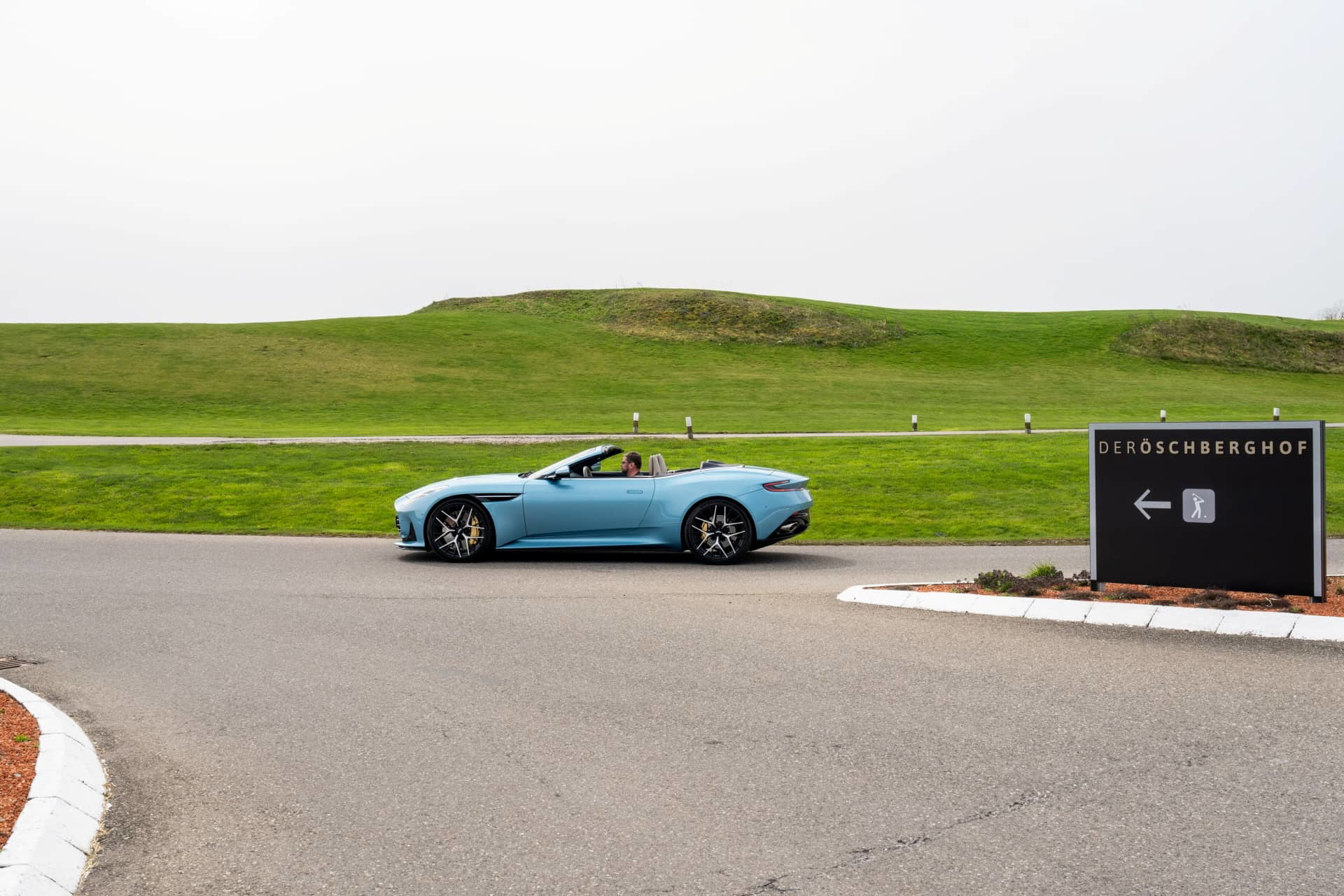 El Aston Martin DB12 Volante se luce en una carretera, mostrando su perfil elegante y deportivo.