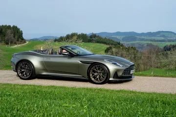 Vista lateral del Aston Martin DB12 Volante 2024 en entorno natural.