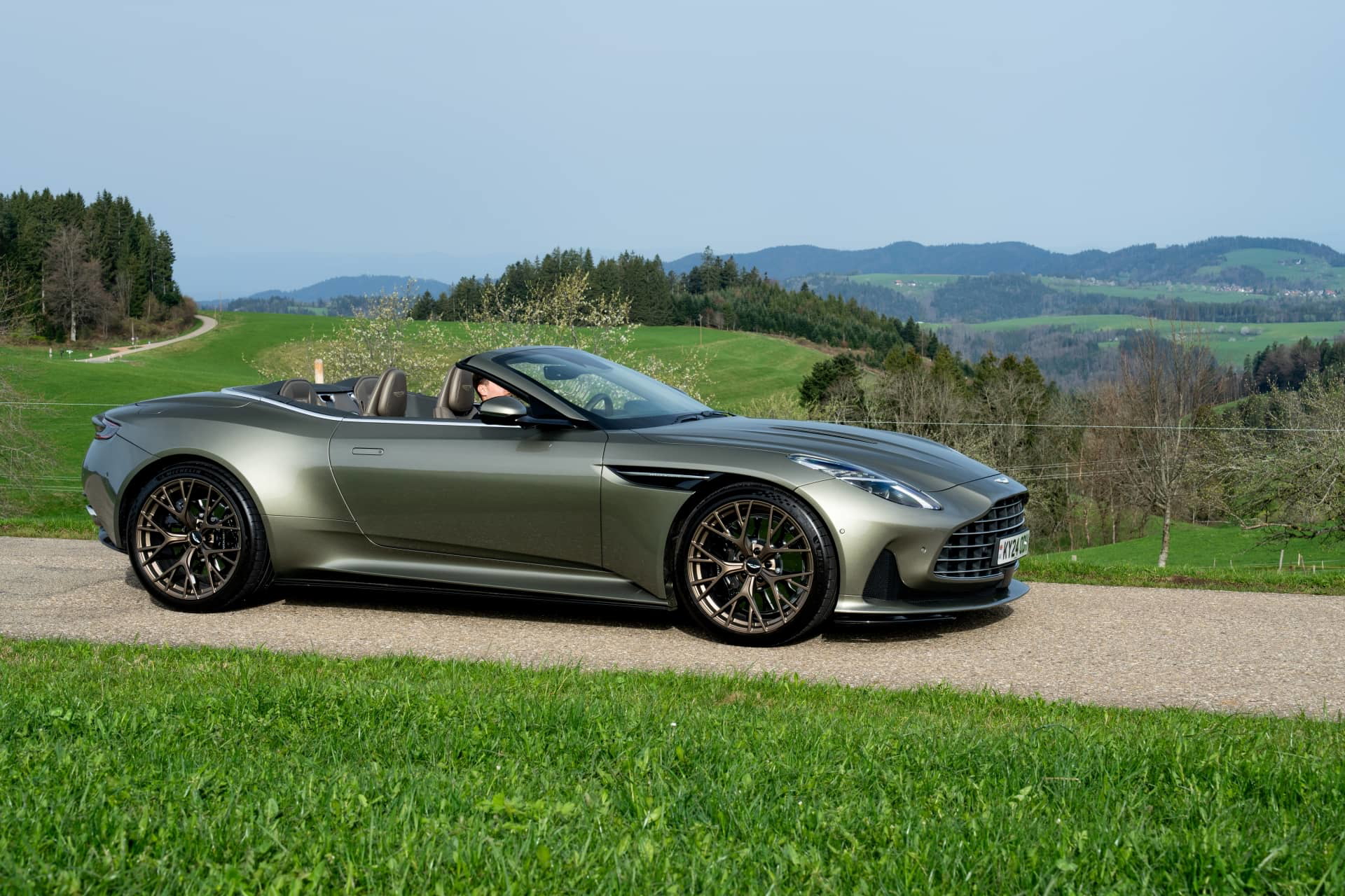 Vista lateral del Aston Martin DB12 Volante 2024 en entorno natural.