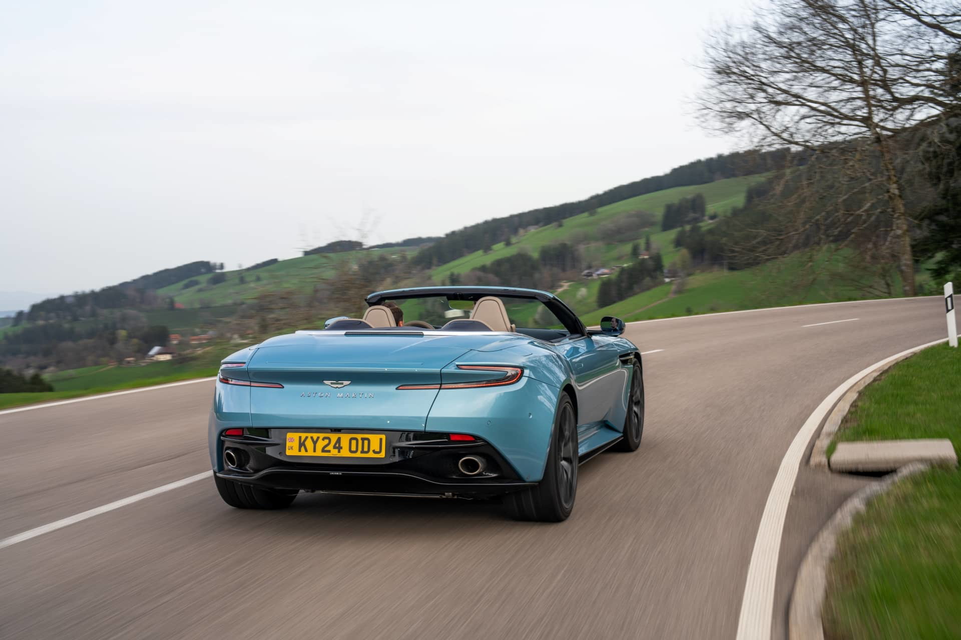 Aston Martin DB12 Volante en movimiento, mostrando su estilizada silueta trasera y lateral.