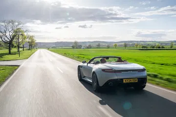 Vista dinámica del Aston Martin DB12 Volante mostrando su elegante diseño trasero y lateral.