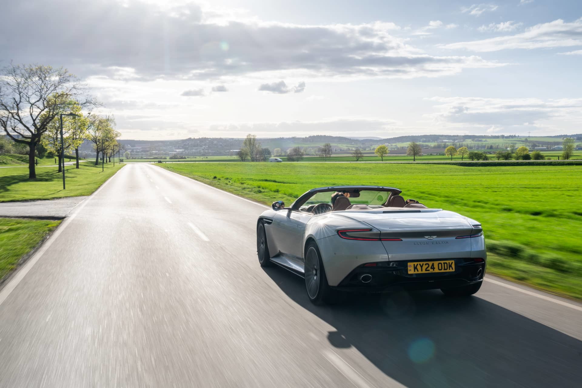 Vista dinámica del Aston Martin DB12 Volante mostrando su elegante diseño trasero y lateral.