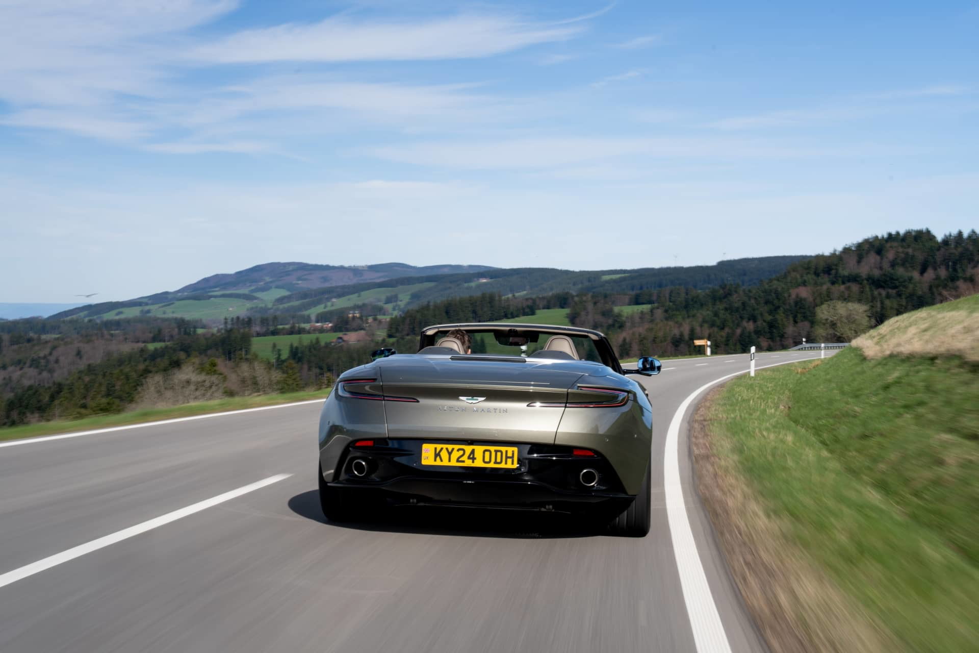 Vista dinámica del Aston Martin DB12 Volante, destacando su diseño trasero y lateral en movimiento.