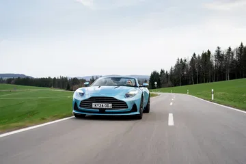 Vista dinámica del Aston Martin DB12 Volante en carretera, destacando su diseño frontal y lateral.