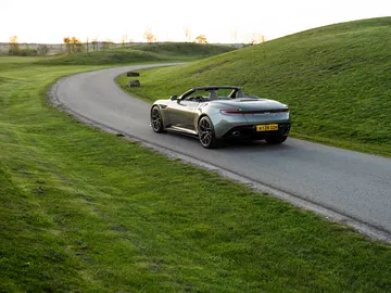 Vista trasera y lateral del Aston Martin DB12 Volante 2024 rodando en carretera secundaria