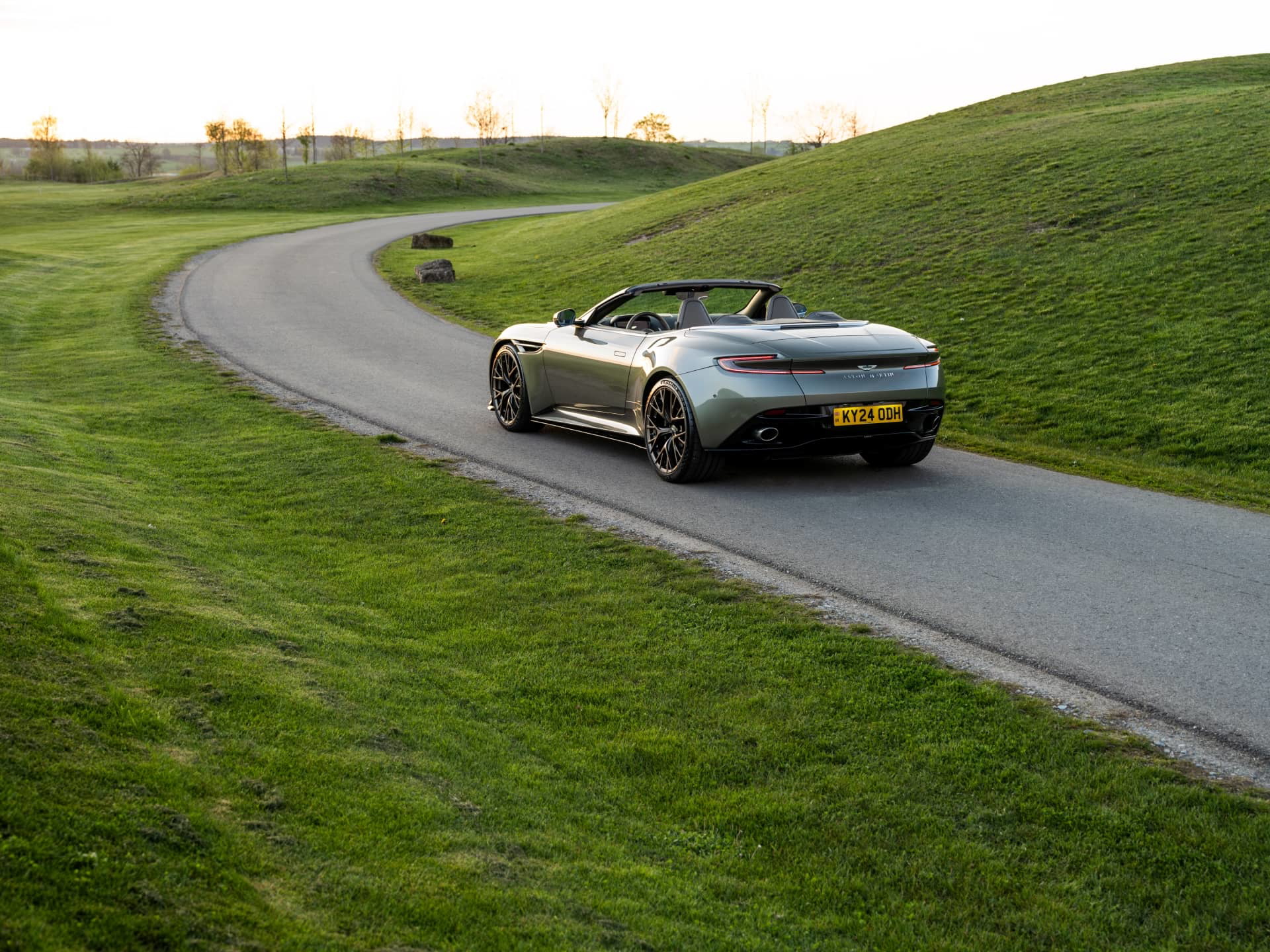 Vista trasera y lateral del Aston Martin DB12 Volante 2024 rodando en carretera secundaria