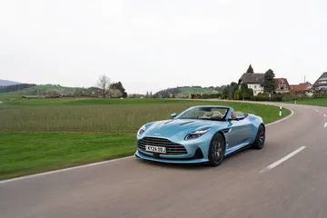 Vista dinámica del Aston Martin DB12 Volante en carretera, resaltando su diseño y deportividad.