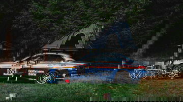 Vista lateral de un BMW Serie 7 con tienda de campaña en el techo, ambientado en una acampada.