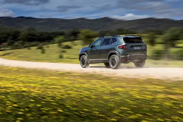 Vista dinámica del Dacia Duster en terreno agreste, destacando su perfil lateral.