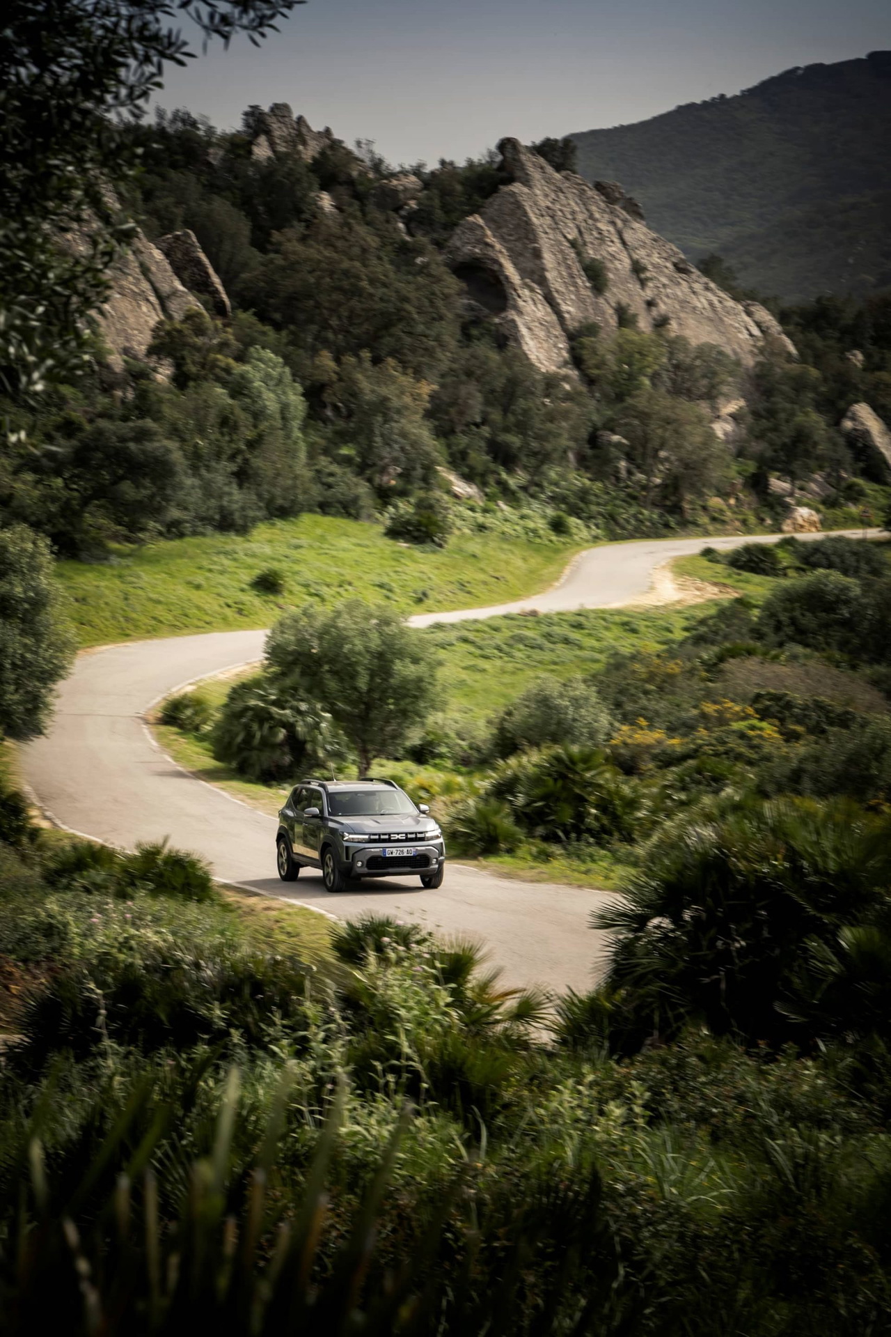 Dacia Duster avanzando por carretera serpenteante en paisaje montañoso.