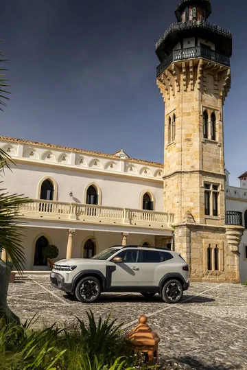 Vista lateral del Dacia Duster aparcado junto a una torre histórica.