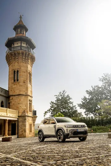 Dacia Duster aparcado junto a torre histórica, vista lateral completa.