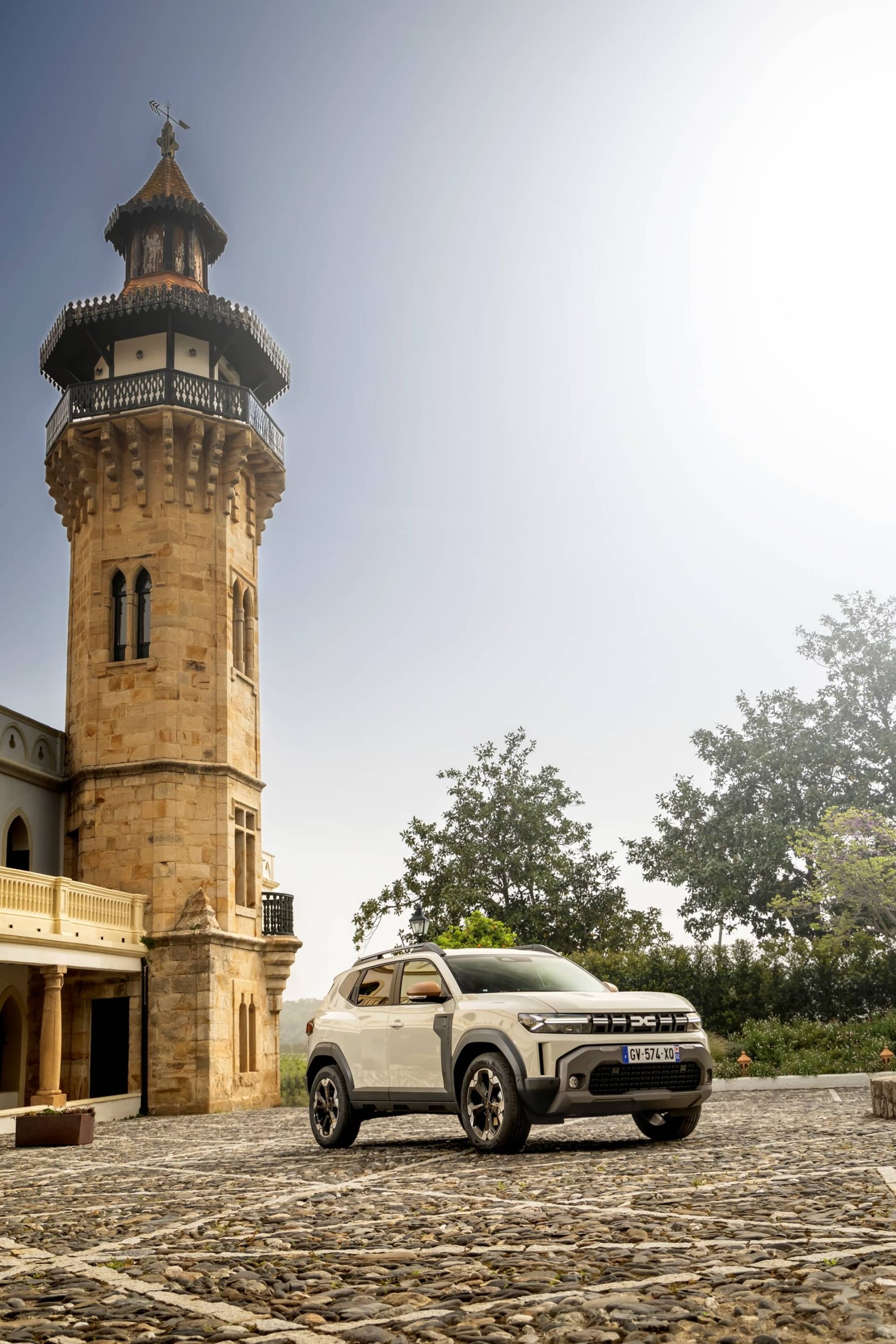 Dacia Duster aparcado junto a torre histórica, vista lateral completa.