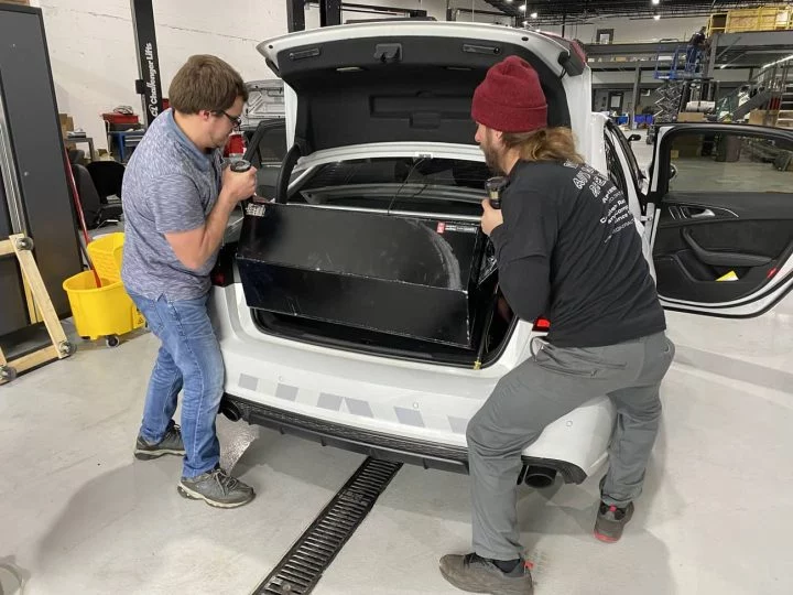 Personal técnico instalando componentes en el maletero del vehículo.
