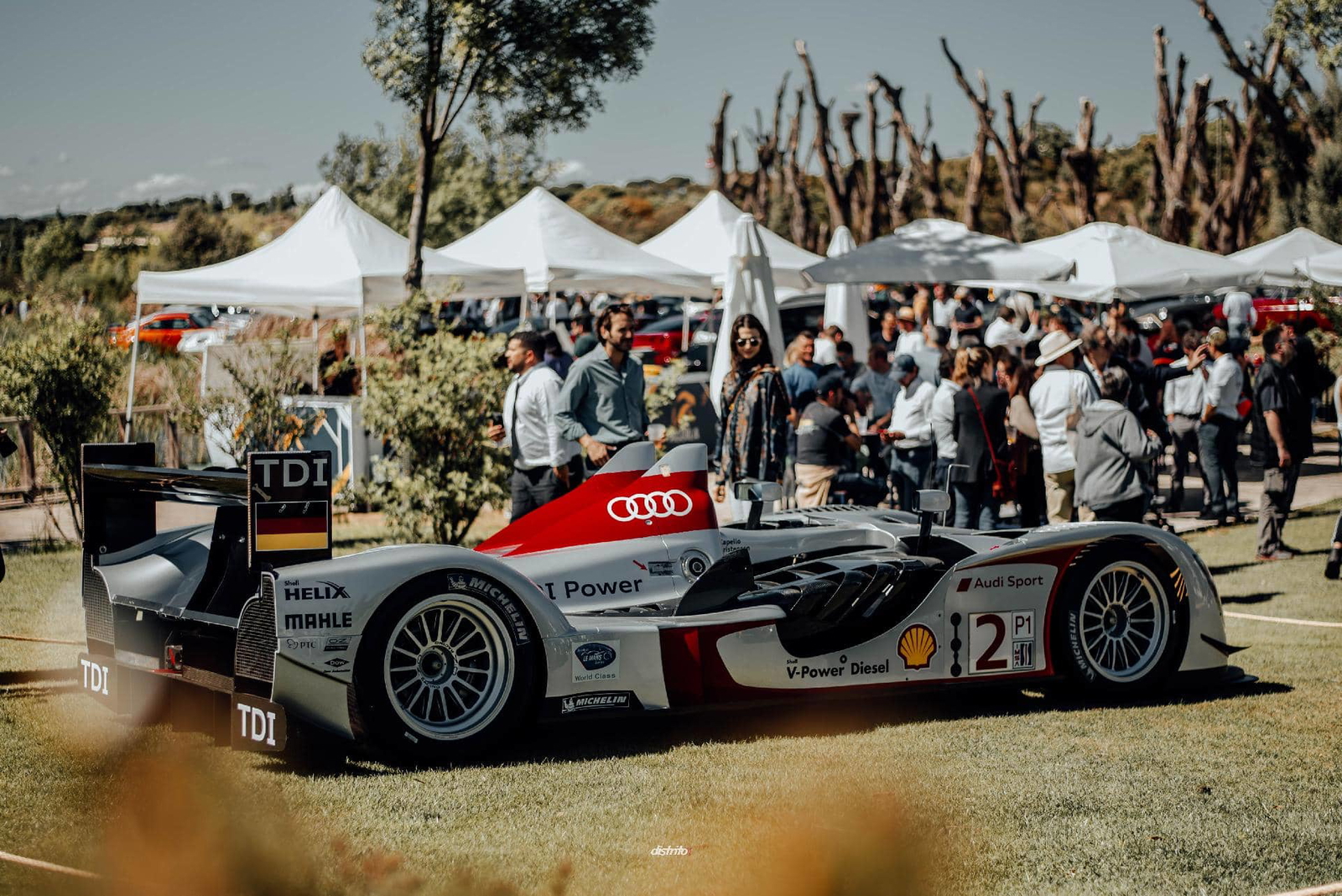 Vista lateral de un Audi de competición en exhibición, rodeado de espectadores. Vista lateral de un Audi de competición en exhibición, rodeado de espectadores.