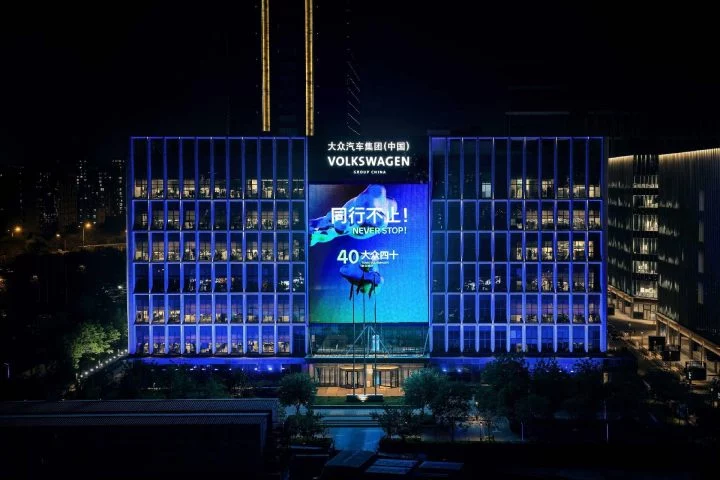 Vista nocturna del edificio de Volkswagen en Beijing, destacando su iluminación y publicidad.
