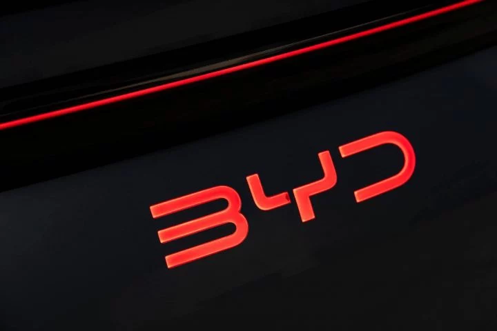 Emblema rojo iluminado de BYD sobre fondo negro, detalle de calidad y diseño.