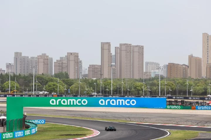 Vista lateral del circuito con el coche de F1 en la distancia bajo un cielo nublado.