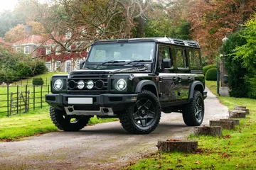 Vista lateral del Ineos Grenadier en un entorno rural, destacando su robustez y diseño clásico.