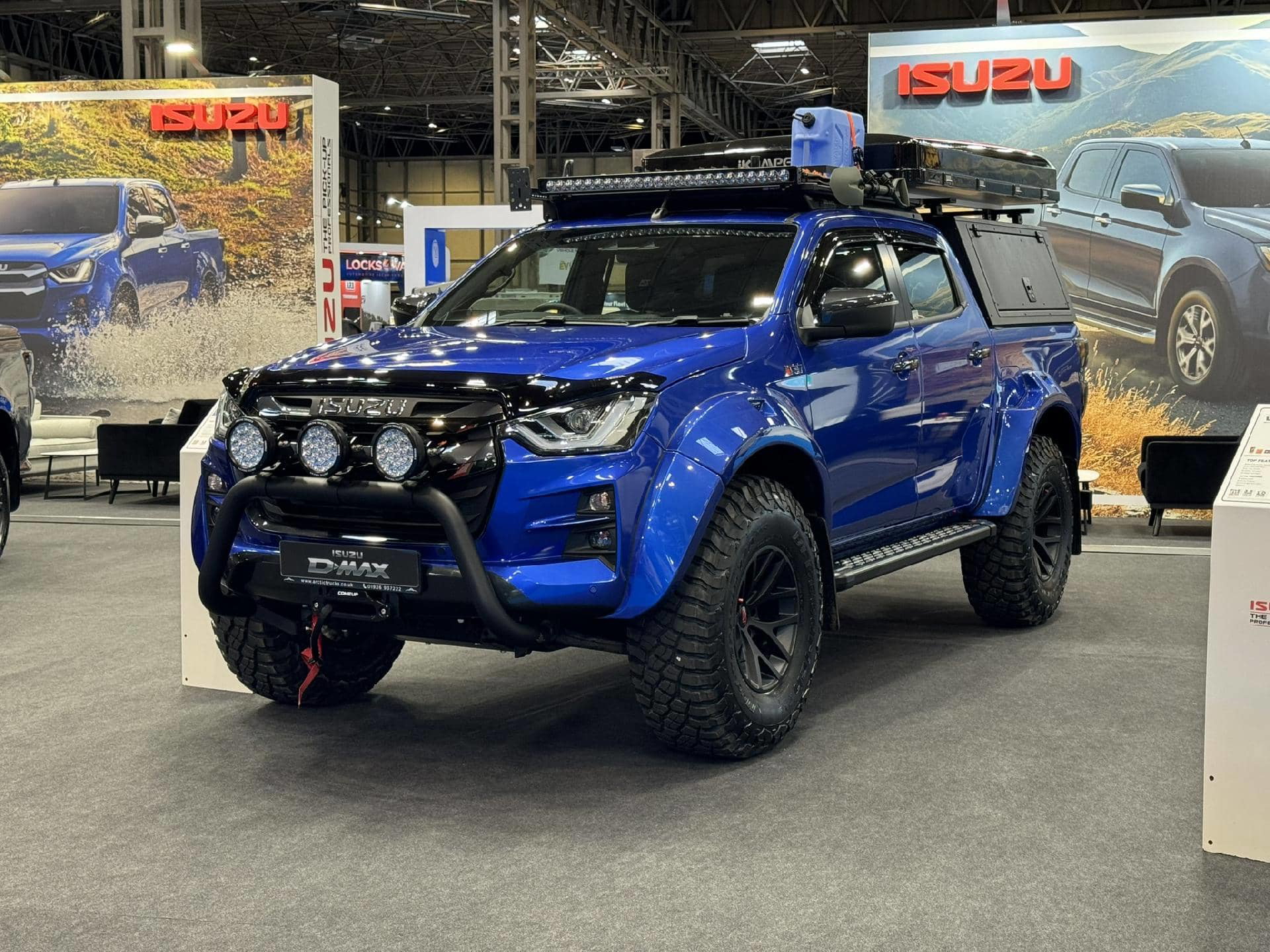 Vista delantera y lateral de un Isuzu D-Max en exhibición, realzando su diseño robusto y funcionalidades off-road.
