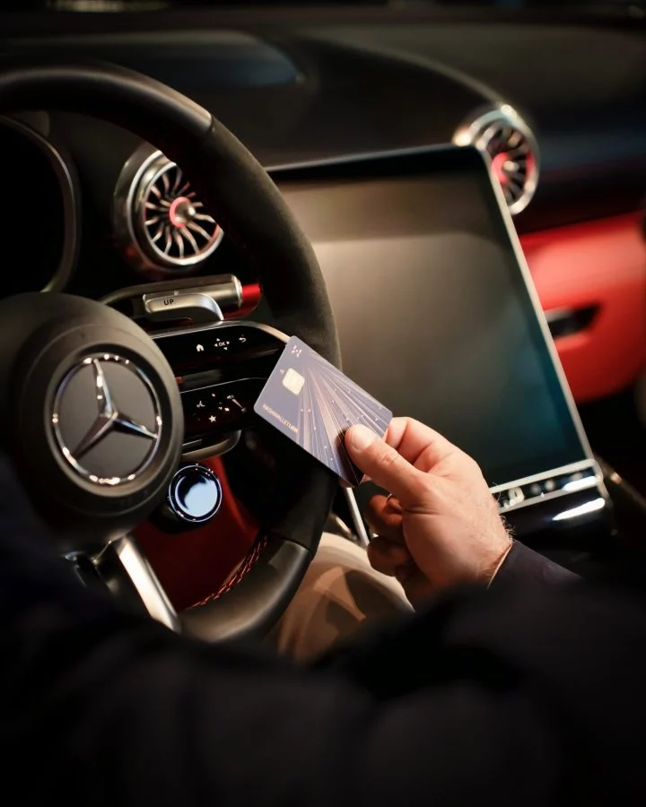 Mano sosteniendo tarjeta cerca del volante Mercedes, enfocado en sistema de pago