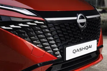 Vista cercana de la parrilla y emblema del Nissan Qashqai 2024 en color rojo.
