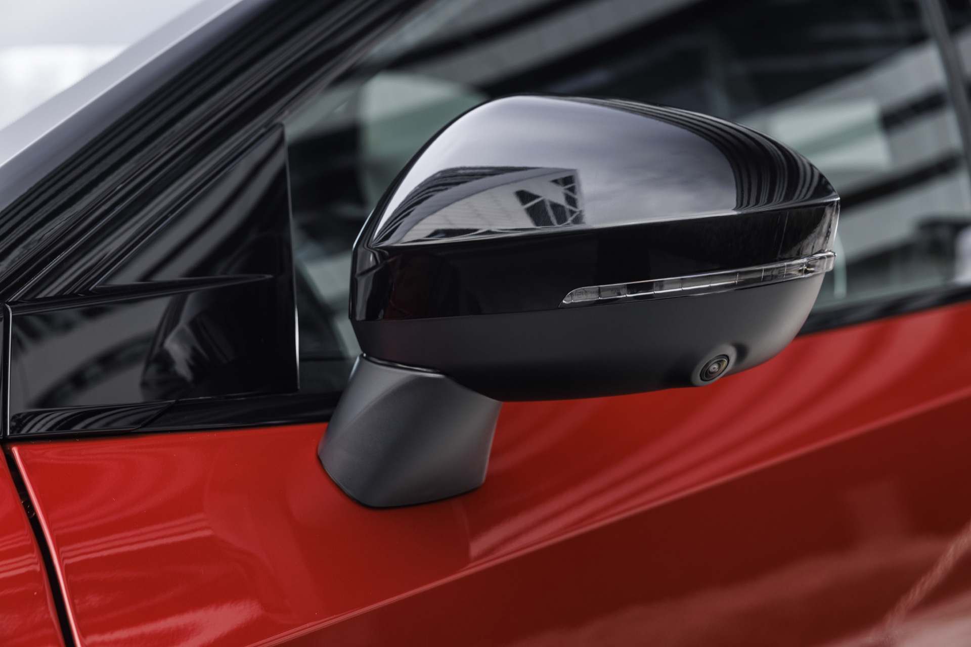 Vista cercana del espejo retrovisor lateral del Nissan Qashqai 2024 en color rojo.
