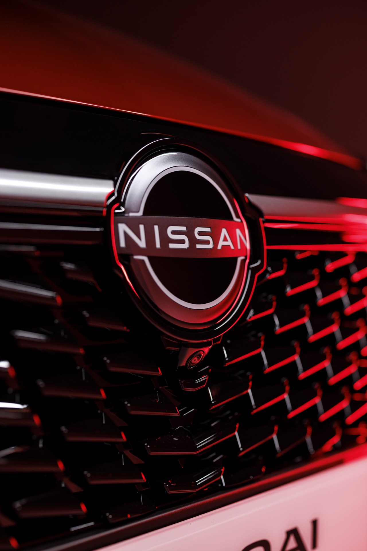 Vista detallada del emblema y parrilla del Nissan Qashqai 2024 en tonalidad roja.